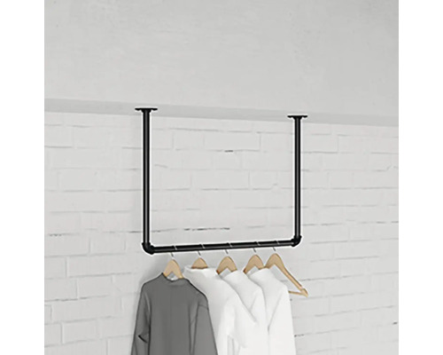 Stojan na šaty z ocelových trubek s visícím oblečením před cihlovou zdí