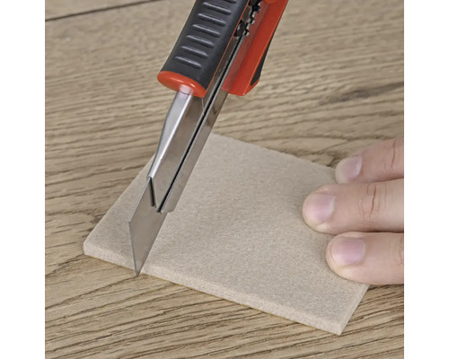 Řezač koberců řeže kus plstěného kluzáku na dřevěné podlaze