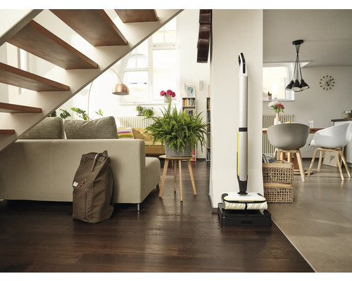 Světlý obývací pokoj se schodištěm, pohovkou, pokojovou rostlinou, batohem a akumulátorovým mopem