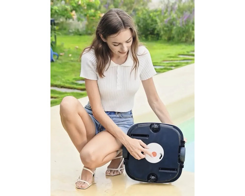 Žena obsluhuje automatický čistič bazénů na zahradě.