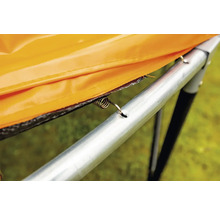 Detailní pohled na pružinu trampolíny, která připevňuje oranžový ochranný kryt k rámu trampolíny.