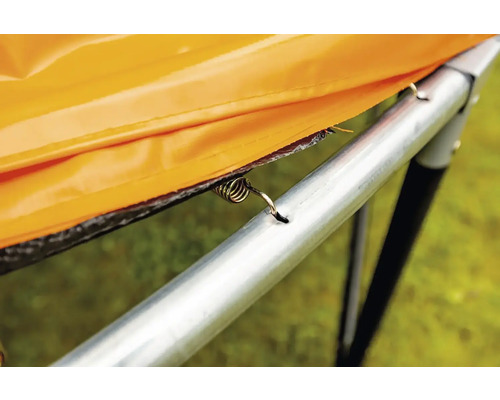 Detailní pohled na pružinu trampolíny, která připevňuje oranžový ochranný kryt k rámu trampolíny.