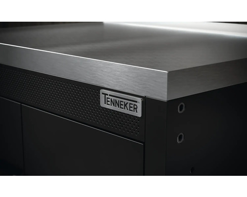 Detailní pohled na pracovní stůl s nerezovou pracovní deskou a logem Tenneker