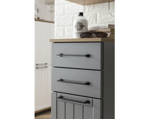 Šedá koupelnová skříňka se třemi zásuvkami a černými úchyty.