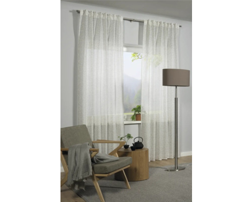 Obývací pokoj s bílými průhlednými závěsy, křeslem, odkládacím stolkem a stojací lampou.