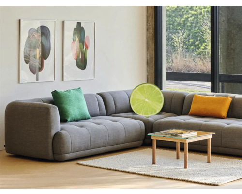 Šedá rohová pohovka s polštáři, konferenční stolek a zarámovaná umělecká díla v obývacím pokoji