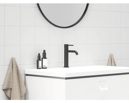 Moderní koupelna s černou vodovodní baterií, bílým umyvadlem a kulatým zrcadlem