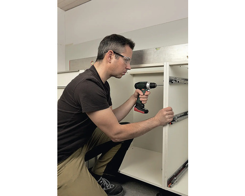 Muž montuje zásuvkové lišty pomocí akumulátorového šroubováku na kuchyňskou skříňku.