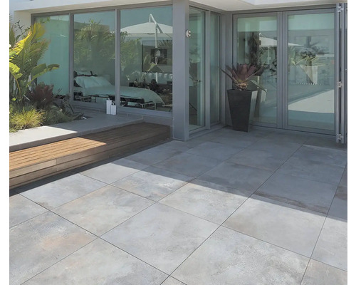 Terasa s velkoformátovými dlaždicemi, dřevěnou lavicí a květináčem před prosklenou fasádou