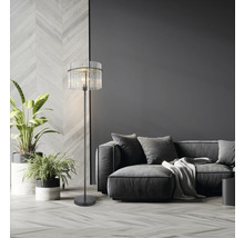 Skleněná a kovová stojací lampa vedle pohovky v obývacím pokoji.