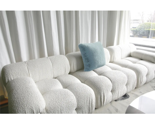 Bílá modulární pohovka se světle modrým polštářem před okny se závěsy