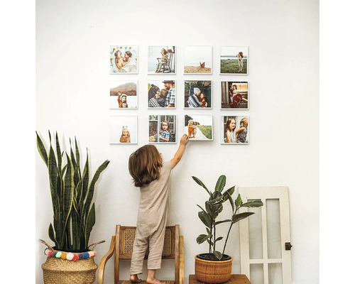 Dítě na židli sahá na fotogalerii na zdi, obklopené rostlinami