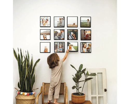 Obývací pokoj s výběrem zarámovaných rodinných fotografií visících na zdi, na které se dívá dítě, spolu s pokojovými rostlinami