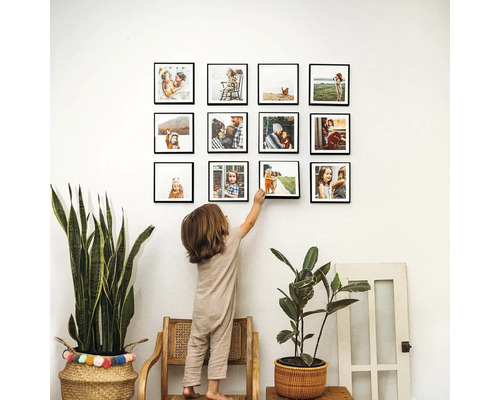 Obývací pokoj se čtvercovými fotorámečky na zdi, zdobený rostlinami a dítětem