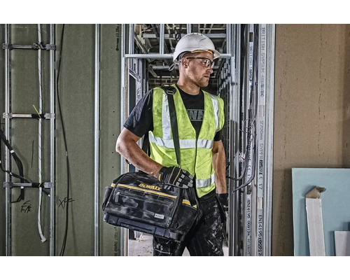 Stavební dělník s brašnou na nářadí značky Dewalt na staveništi.