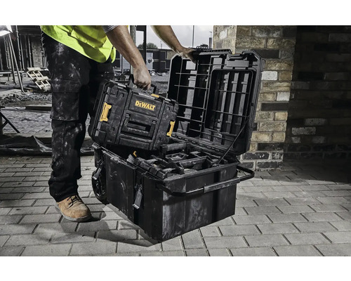 Muž pokládá kufřík na nářadí značky DeWalt na jiný kufřík na nářadí na staveništi