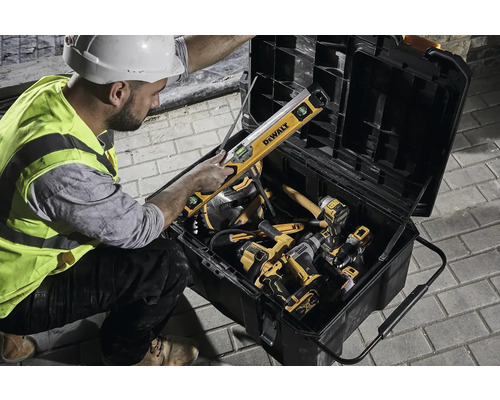 Stavební dělník ukládá nářadí, jako je vodováha a akumulátorové vrtačky, do kufříku na nářadí.