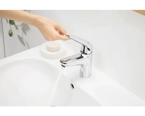 Osoba ovládá chromovanou vodovodní baterii na bílém umyvadle