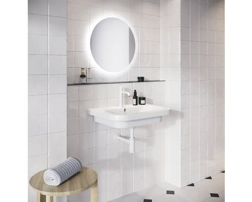 Koupelna s bílým umyvadlem, kulatým zrcadlem s osvětlením a ručníkem na stoličce