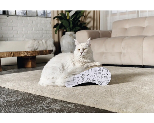Bílá kočka leží na škrabadle s kočičími motivy v světlém obývacím pokoji.