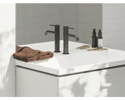 Koupelnové umyvadlo s baterií, ručníkem, hřebeny a pečujícími produkty na bílém povrchu.