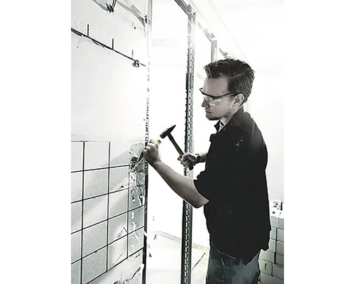 Muž odstraňuje dlaždice ze zdi pomocí kladiva a dláta.