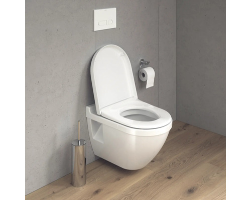 Závěsné WC s otevřeným splachovacím kruhem, ovládáním splachování, držákem toaletního papíru a WC štětkou v koupelně.