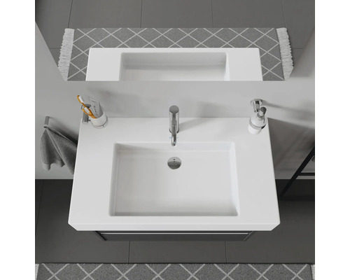 Pohled shora na bílé umyvadlo s baterií, dávkovačem mýdla a držákem na zubní kartáčky v koupelně