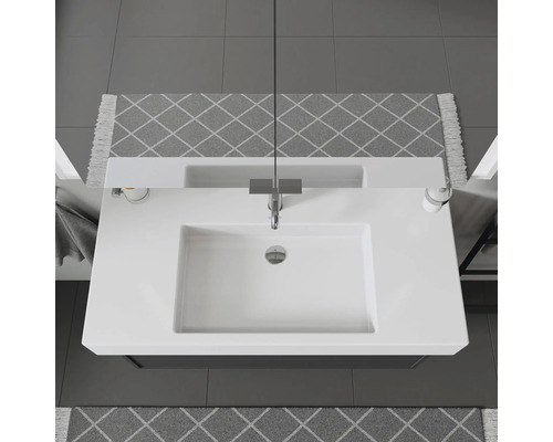 Pohled shora na umyvadlo s vodovodní baterií, dávkovačem mýdla a vzorovanými koberci v koupelně.