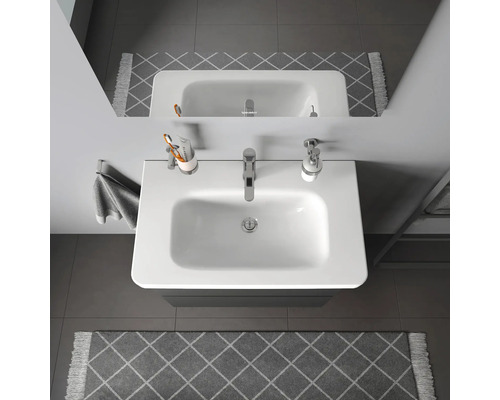 Pohled shora na umyvadlo v koupelně s vodovodní baterií, dávkovačem mýdla, kelímkem na zubní kartáčky a ručníkem