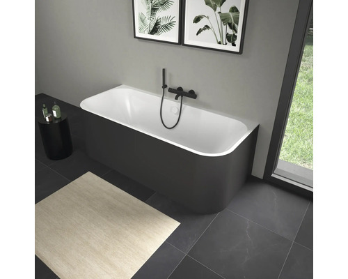 Volně stojící vana s černou armaturou v koupelně s uměleckými díly a kobercem.