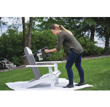 Žena stříká barvu na zahradní židli Adirondack pomocí stříkací pistole.