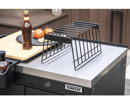 Kovová odkládací mřížka na grilovací stanici s lahví, rajčaty a krájecí deskou