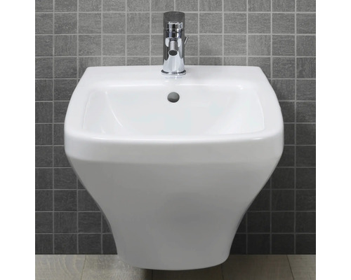 Bílé nástěnné umyvadlo s chromovou baterií před šedou obkládačkovou stěnou