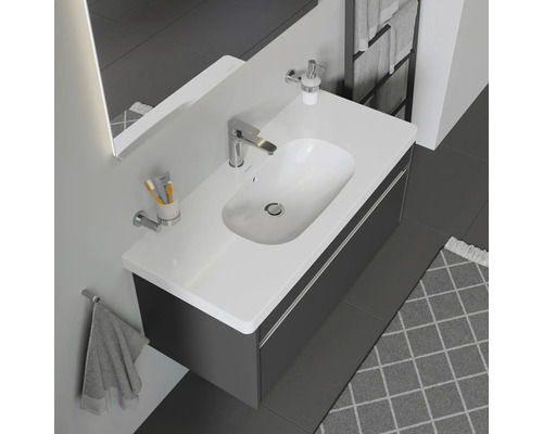 Moderní koupelna s umyvadlem, skříňkou, baterií, dávkovačem mýdla, ručníkem a dalším koupelnovým příslušenstvím.