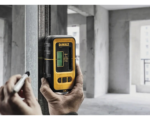 Osoba používá čárový laser DeWalt na kovovém sloupku v hrubé stavbě k označení perem.