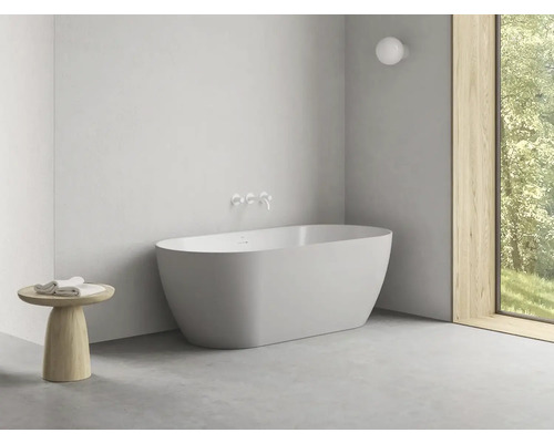 Volně stojící vana v světlé koupelně s oknem a malým stolem s ručníky