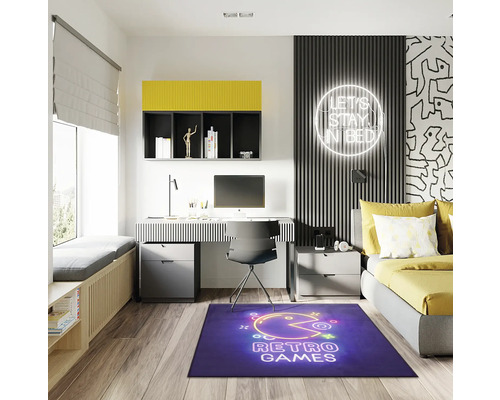 Moderní studentský pokoj se stolem, postelí a modrým kobercem s motivem retro her.