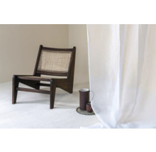 Scéna s tmavou dřevěnou židlí s ratanovým sedákem, džbánem a šálkem na podnosu a průhledným závěsem.