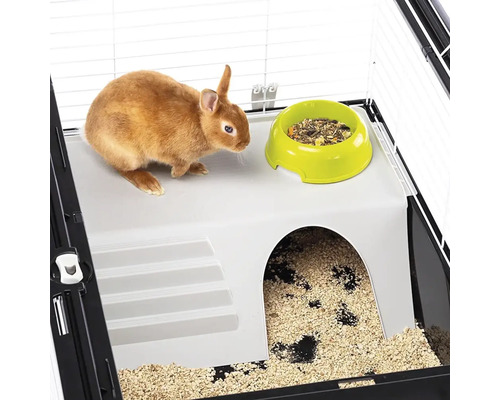 Malý králík v kleci s miskou na krmivo a úkrytem