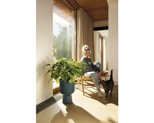 Žena se sluchátky sedí vedle rostliny v květináči v obývacím pokoji