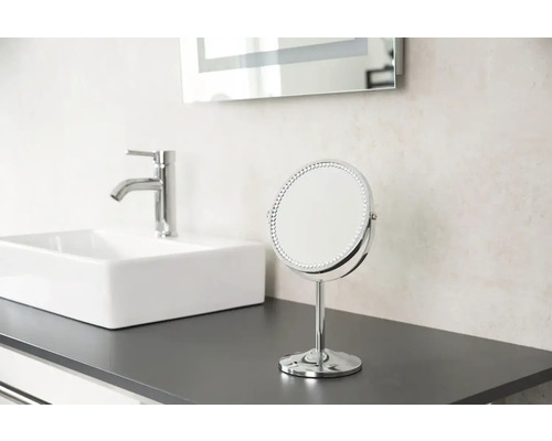 Na umyvadle stojí zrcadlo, umyvadlo a kohoutek.