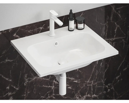 Bílé umyvadlo s baterií, kosmetickými produkty a odpadní trubkou před mramorovou stěnou.