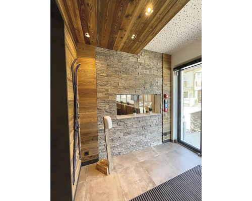 Interiér s obložením ze dřeva a kamene, lyže na zdi a dávkovač dezinfekce