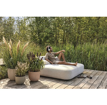 Scéna s osobou odpočívající na zahradní pohovce venku, obklopené květináči a zelení