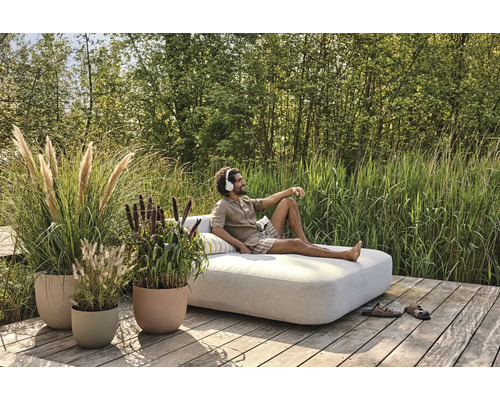 Scéna s osobou odpočívající na zahradní pohovce venku, obklopené květináči a zelení