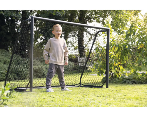 Chlapec stojí před fotbalovou brankou na zahradě.