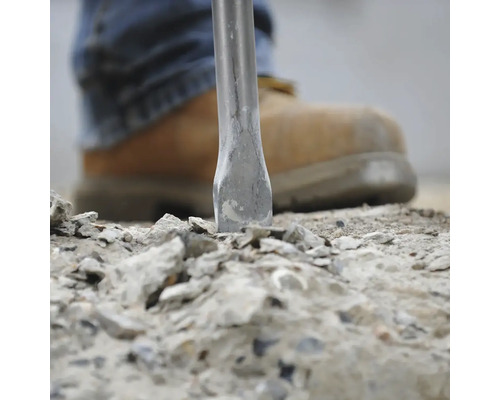 Dláto opracovává kamenný materiál s pracovní obuví v pozadí