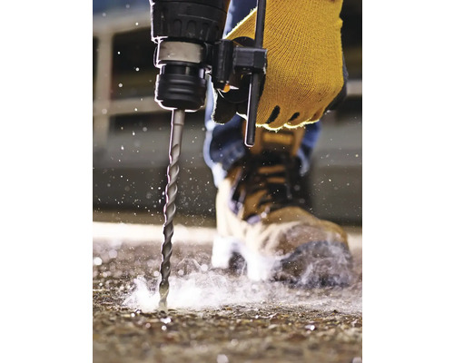 Osoba vrtá vrtačkou do podlahy, má na sobě ochranné rukavice a bezpečnostní obuv.