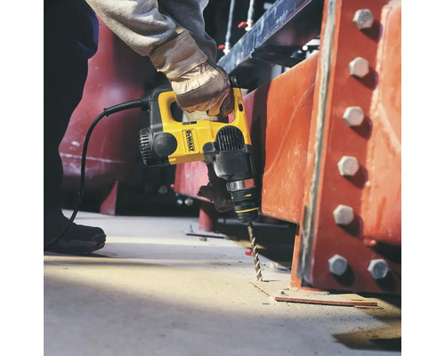 Osoba vrtá do betonové podlahy žlutým vrtacím kladivem značky DeWalt.